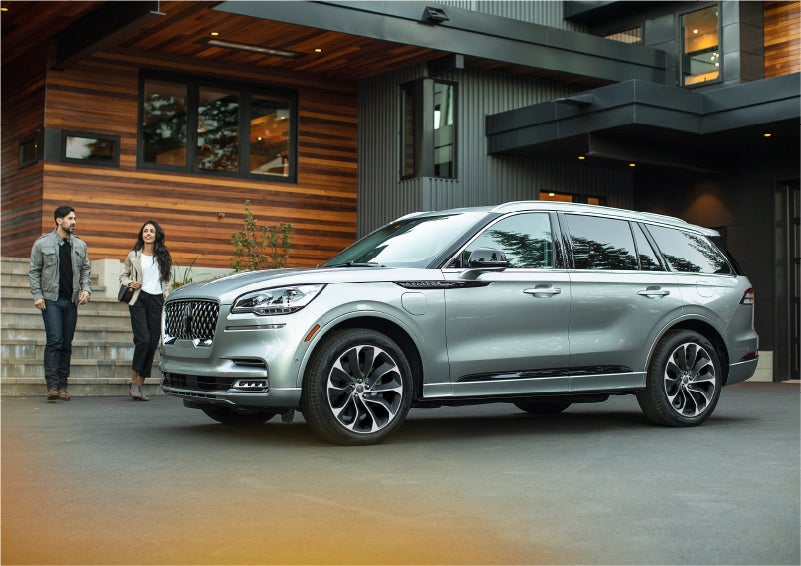 A couple approach a 2023 Lincoln Aviator® Grand Touring model parked in the driveway of a modern home | Uptown Lincoln in Wauwatosa WI