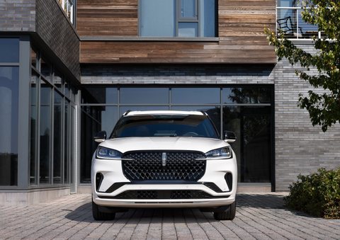 A white 2025 Lincoln Aviator® SUV is shown parked outside a modern building with gray brick and wood accents. | Uptown Lincoln in Wauwatosa WI