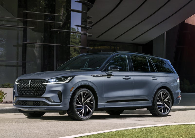 A gray 2025 Lincoln Aviator® SUV is parked outside a modern building showcasing the driver’s side of the vehicle. | Uptown Lincoln in Wauwatosa WI