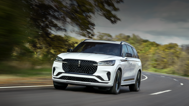 A white 2025 Lincoln Aviator® SUV is being driven down a road lined with trees. | Uptown Lincoln in Wauwatosa WI