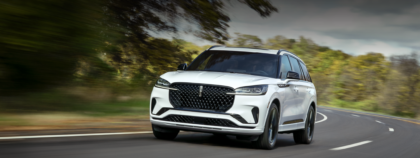A white 2025 Lincoln Aviator® SUV is being driven down a road lined with trees. | Uptown Lincoln in Wauwatosa WI
