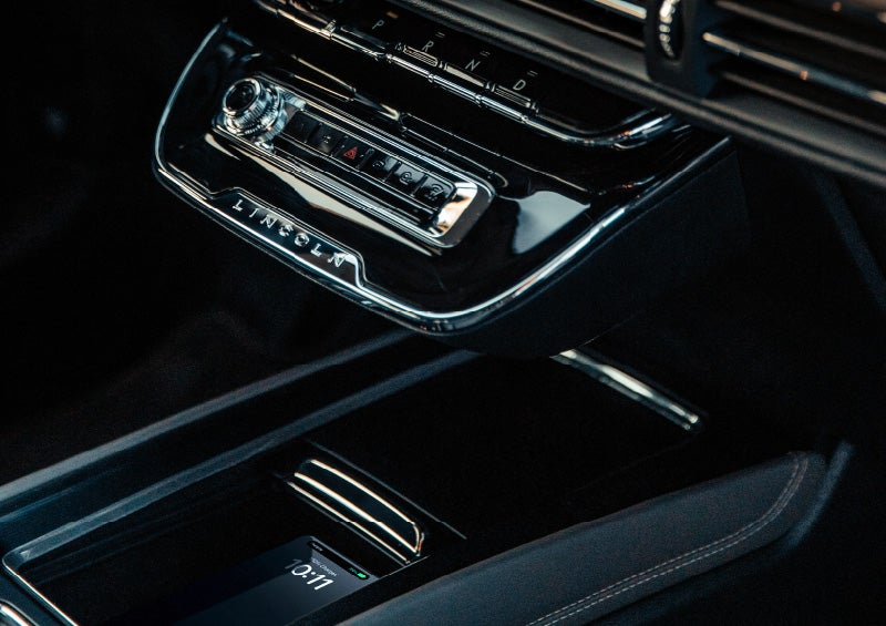 A smartphone rests on the wireless charging pad in the front center console cubby.