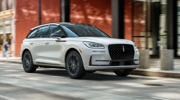 A white 2025 Lincoln Corsair® SUV with the Jet Appearance Package is being driven through a city.| Uptown Lincoln in Wauwatosa WI
