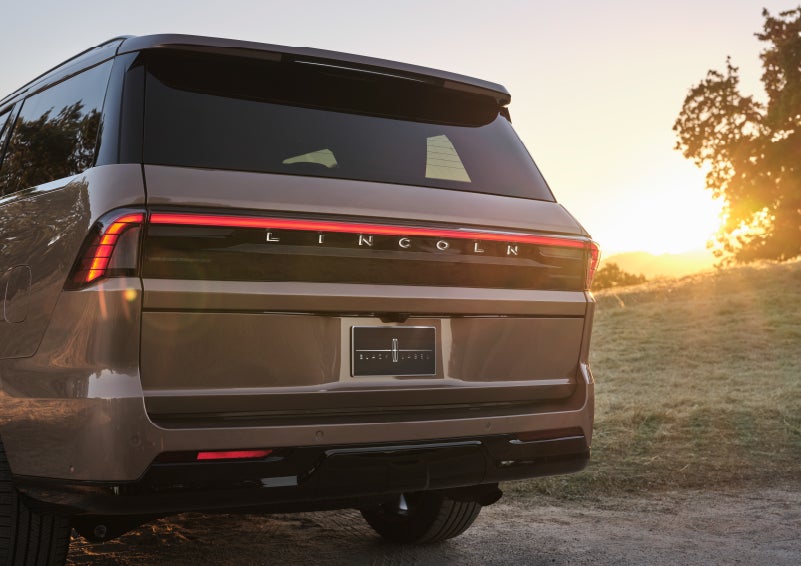 A woman is approaching a 2025 Lincoln Navigator® SUV with an elegant clear purse displaying a smartphone and lipstick.