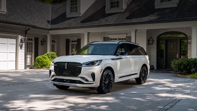 A white 2026 Lincoln Aviator® SUV is parked in the driveway of a luxury home. | Uptown Lincoln in Wauwatosa WI
