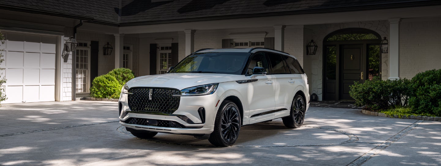 A white 2026 Lincoln Aviator® SUV is parked in the driveway of a luxury home. | Uptown Lincoln in Wauwatosa WI
