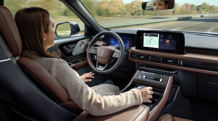 A 2027 Lincoln Aviator® SUV is being driven hands-free on a highway lined with trees. | Uptown Lincoln in Wauwatosa WI