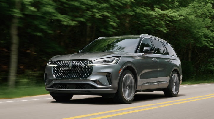 A 2027 Lincoln Aviator® SUV is being driven down a road lined with trees. | Uptown Lincoln in Wauwatosa WI