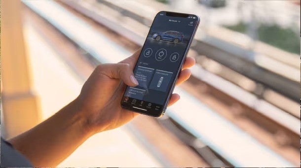Hand holding a smartphone displaying a car control app for a blue Lincoln car, with lock, unlock, and start buttons.