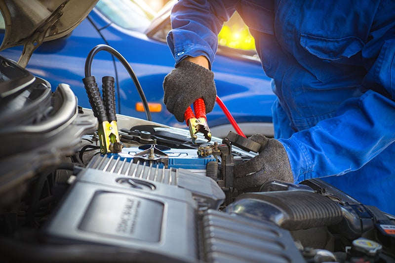Technician using jumper cables to test or service a vehicle battery under the hood during automotive maintenance