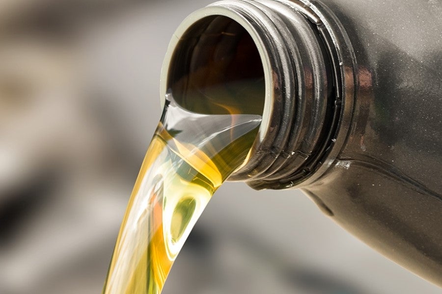 Close-up of golden engine oil being poured from a motor oil container, illustrating a vehicle oil change or engine maintenance service
