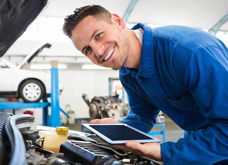 Automotive technician using a tablet to perform vehicle diagnostics and maintenance in a service center
